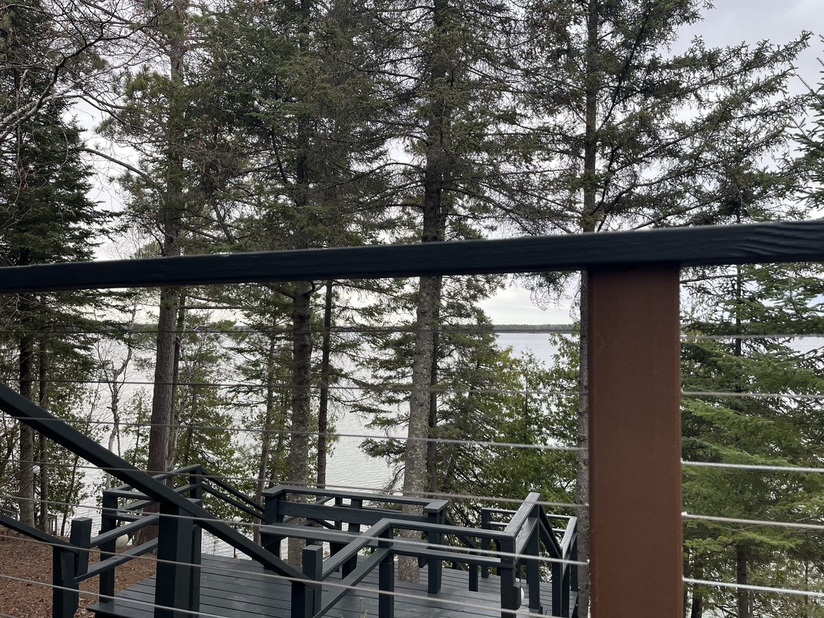 Deck railing overlooking Minnesota lake through pine trees - JAM Custom Carpentry